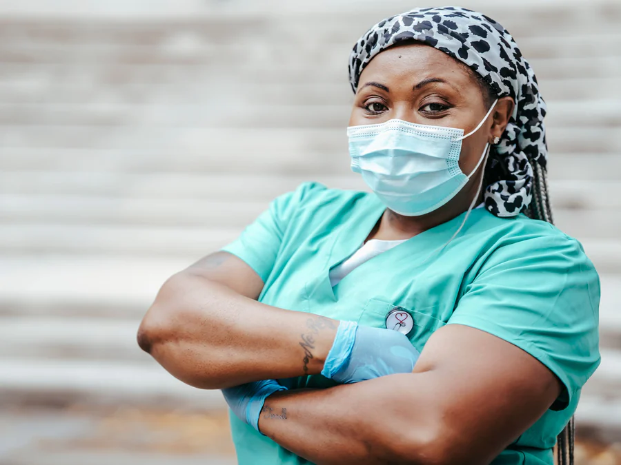 A nurse in scrubs standing outdoors with her arms folded